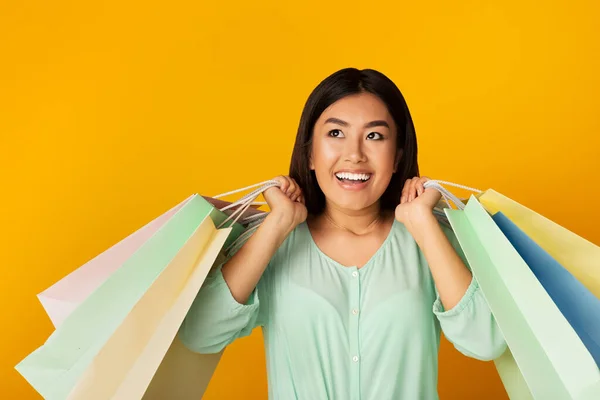 Glada asiatiska kvinna med Shopper väskor Posing över gul bakgrund — Stockfoto