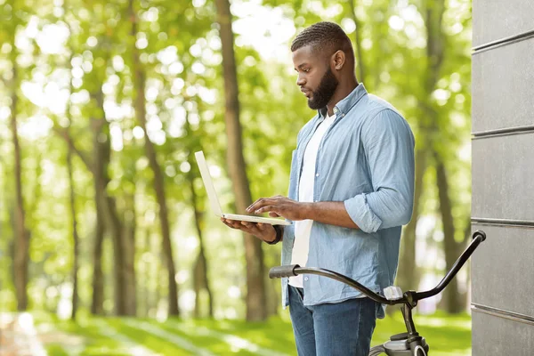잘생긴 흑인 이 야외에서 랩탑을 들고 공원에서 서 WiFi 를 확인하고 있습니다 — 스톡 사진