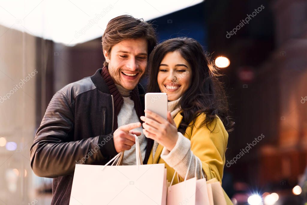 Loving couple using phone after shopping in mall