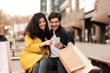 Sevgili çift bankta telefon kullanıyor.
