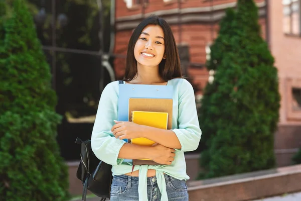 Sorrindo asiático estudante menina com mochila e cadernos de trabalho sobre faculdade fundo — Fotografia de Stock