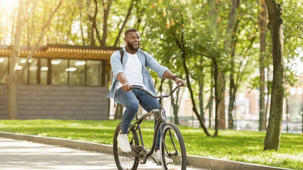 Primeiro passeio. Excitado afro homem com mochila andar de bicicleta no parque — Fotografia de Stock