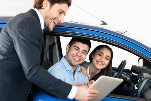Casal feliz comprando carro conversando com vendedor sentado em automóvel — Fotografia de Stock