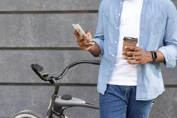 Ubrecognizable homem negro de pé perto de bicicleta, relaxante com café e smartphone — Fotografia de Stock