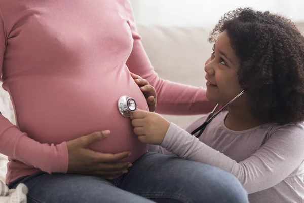 小非洲裔女儿用听诊器听她怀孕的妈妈们的肚子 — 图库照片