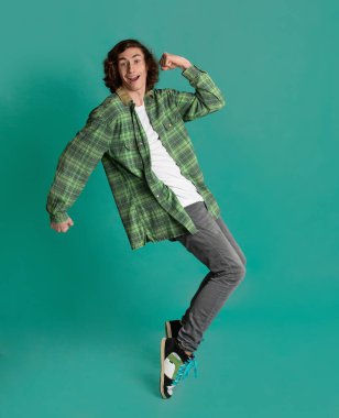 Turkuaz arka planda parmak uçlarında duran mutlu genç adam.