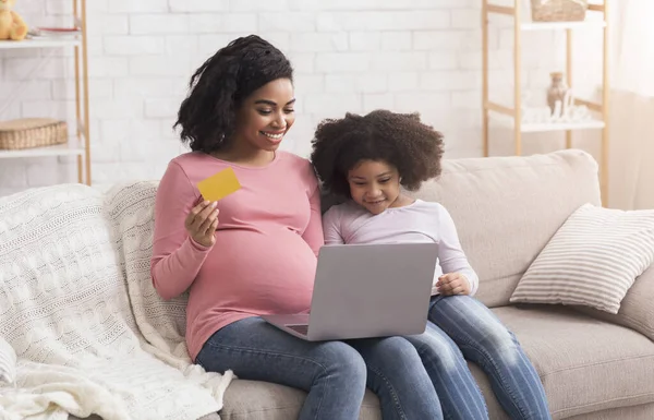 Беременная мама с ноутбуком и кредитные карты покупки в Интернете с дочерью — стоковое фото