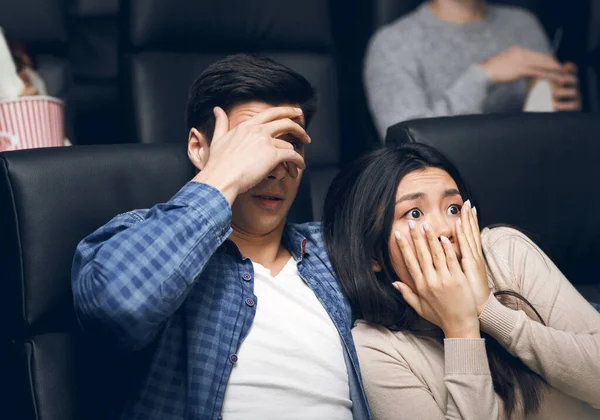 Joven con su novia cerrando caras de terror mientras ve una película de terror en el cine —  Fotos de Stock