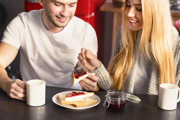 Happy guy and his girlfriend having toasts with jam and coffee for breakfast in kitchen — Stock Photo, Image