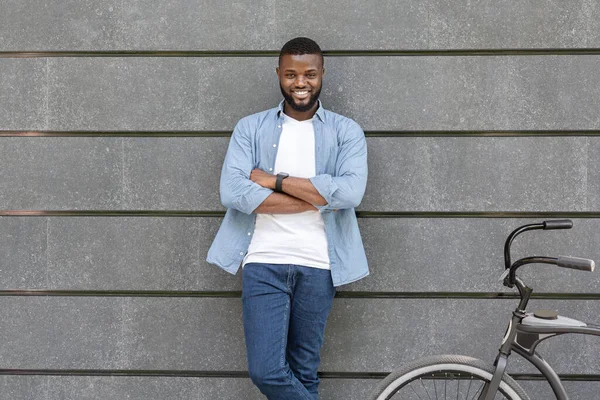Щасливий чорний чоловік спирається на стіну і стоїть біля свого велосипеда — стокове фото