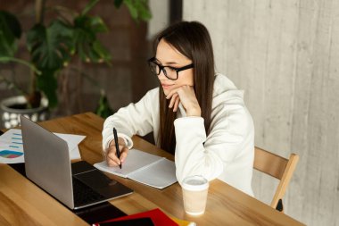 Freelance woman looks at laptop and takes notes