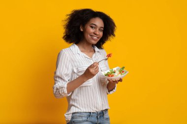 Smiling Afro Woman Eating Fresh Vegetable Salad Standing On Yellow Background