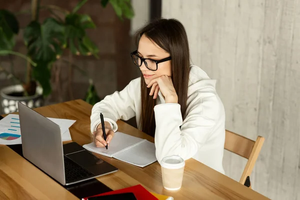 Freelance woman looks at laptop and takes notes — 图库照片