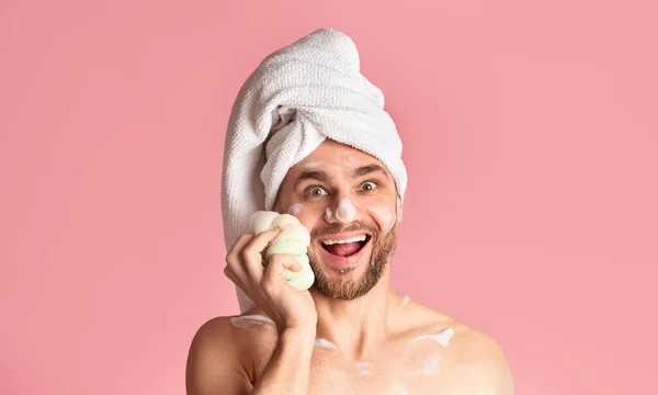 Guy in foam rubs face sponge in bathroom — Stockfoto