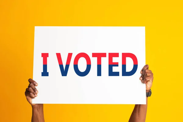 African American citizen holding banner with words I VOTED on orange background, closeup — стокове фото