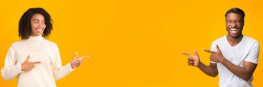 Cheerful African American man and woman pointing at blank space on yellow studio background, panorama