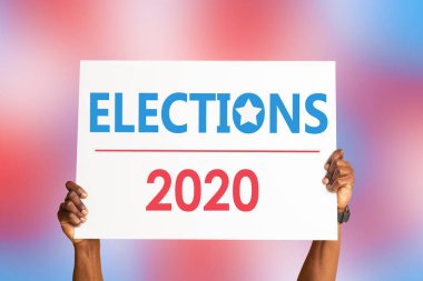 African American citizen holding sign that says ELECTIONS 2020 on colorful background, closeup