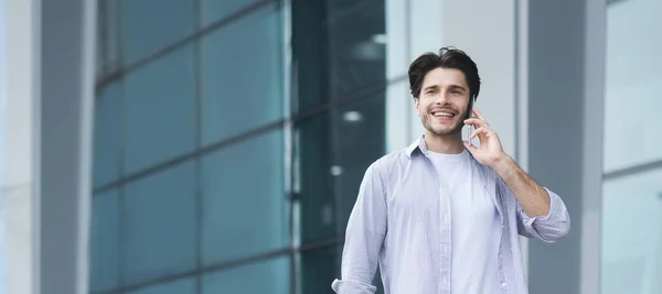 Comunión moderna. Guapo joven hablando en el teléfono móvil al aire libre —  Fotos de Stock