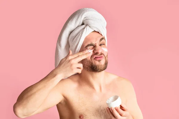 Cute young man grimacing and smears face cream — Stok fotoğraf