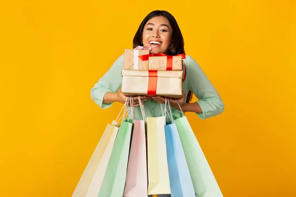 Happy Girl Holding Wrapped Gifts And Shopper Bags, Yellow Background — Stockfoto
