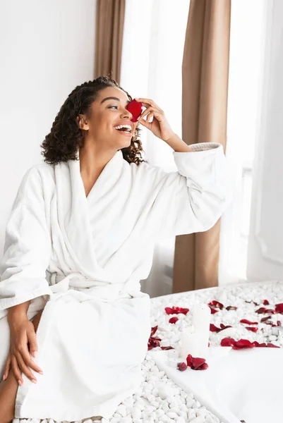 Wanita hitam ceria di jubah mandi bermain dengan kelopak mawar — Stok Foto
