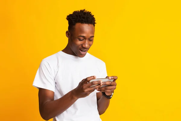 Homem americano africano alegre usando celular no amarelo — Fotografia de Stock