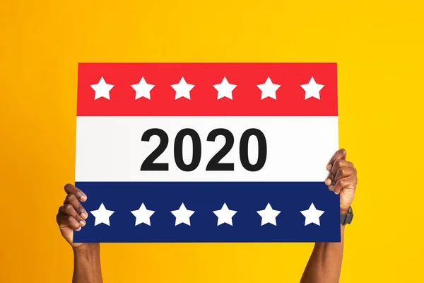 Молодой черный мужчина держит плакат со звездами и номером 2020 на оранжевом фоне — стоковое фото