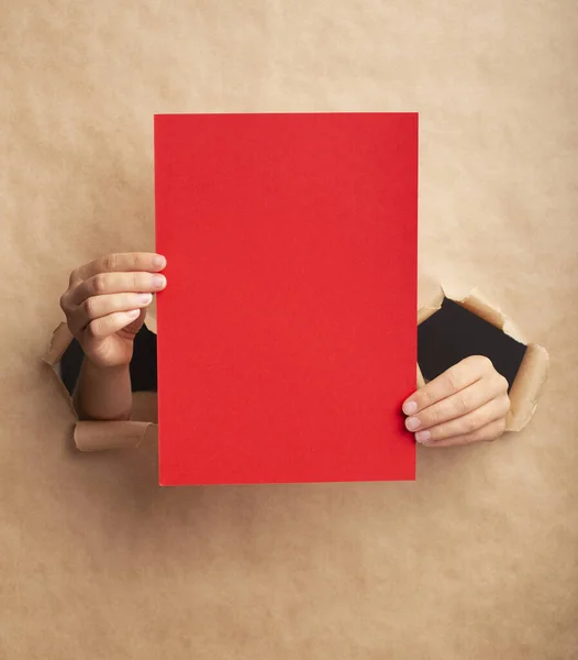Unrecognizable lady holding red sheet with empty space through ripped craft paper — Stock fotografie