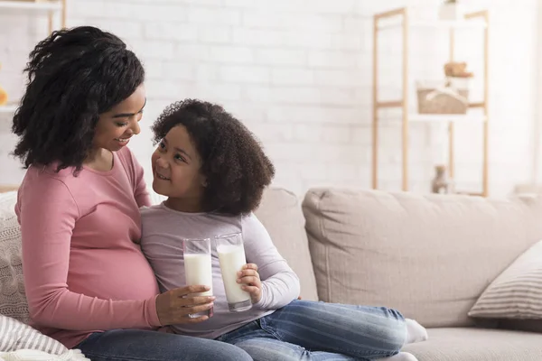 Маленькая африканская американская девочка и ее беременная мать пьют молоко вместе — стоковое фото