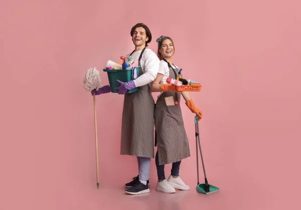 Happy young couple with lots of detergents posing over pink background — Stockfoto