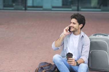 Milenyum adamı cep telefonuyla konuşuyor ve havaalanının dışında kahve içiyor.