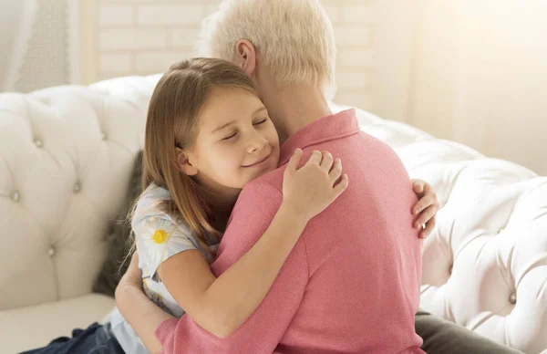 Cute little girl embracing her grandmother in living room — Stock Photo, Image