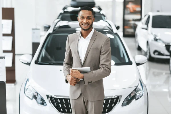 Auto vendedor homem sorrindo para câmera de pé no centro de automóveis — Fotografia de Stock