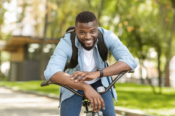 Homem afro-americano feliz sentado na bicicleta e posando para câmera — Fotografia de Stock