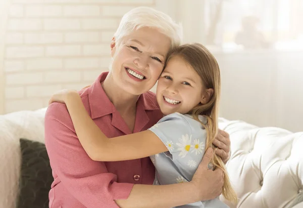 Happy granny with granddaughter hugging on sofa at home