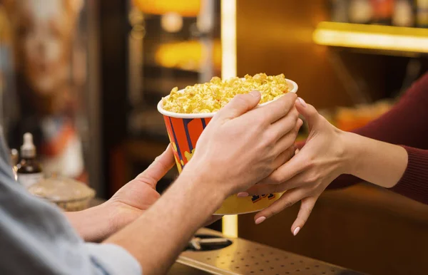 Mladý muž kupující popcorn od prodavačky v kinosálu lobby, detailní záběr rukou — Stock fotografie