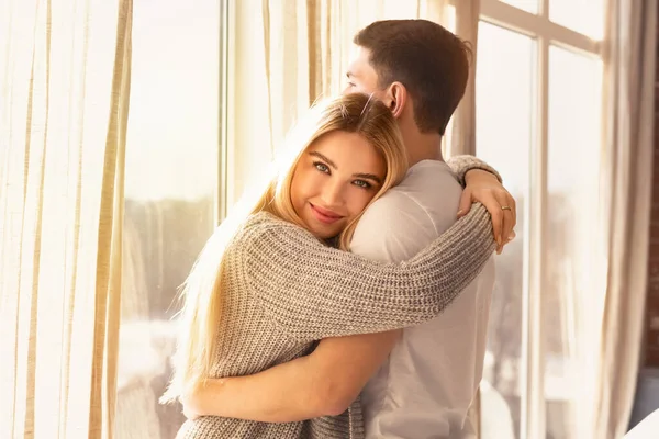 Young guy and girl hugging near window in sunlit room — Stockfoto