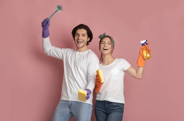 Joyful couple with sponge, detergent and brush posing over pink background — Stock Photo, Image