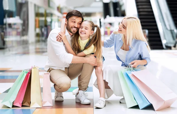 Jovens pais alegres abraçando a filhinha sentada na loja do shopping — Fotografia de Stock