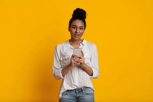 Fille afro excitée avec Smartphone dans les mains sur fond jaune — Photo