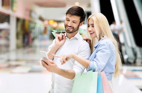 Małżonkowie korzystający ze smartfona wyszukiwania sprzedaży i ofert stojących w centrum handlowym — Zdjęcie stockowe
