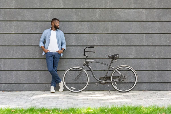 Afro hombre con elegante bicicleta posando sobre gris pared urbana — Foto de Stock