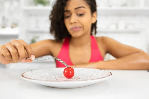 Malheureux afro femme regardant minuscule tomate sur une assiette — Photo