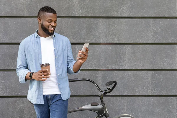 Preto cara de pé perto de bicicleta, mensagens de texto no smartphone e beber café — Fotografia de Stock