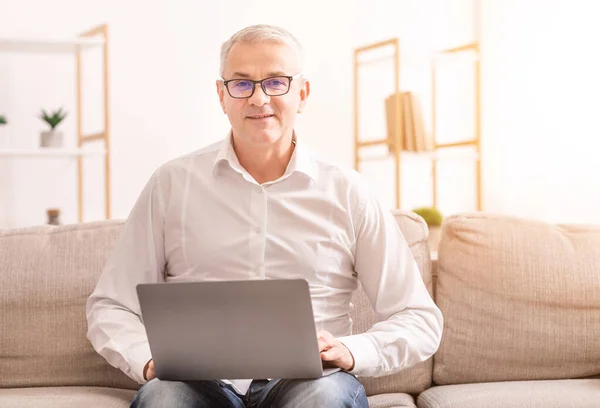 Yaşlı Adam Dizüstü bilgisayar kullanıyor Koltukta oturuyor — Stok fotoğraf