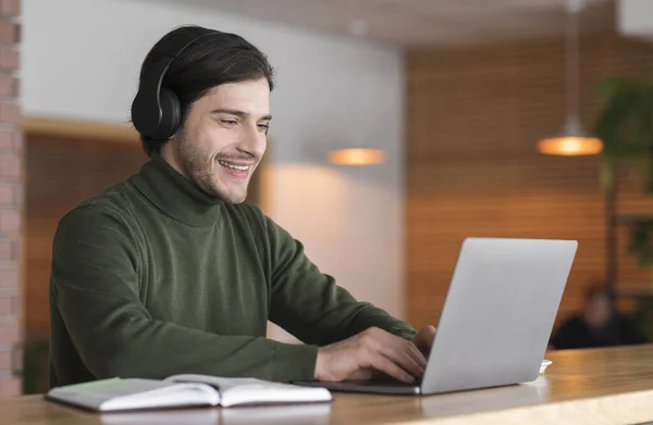 Joven hombre positivo en auriculares inalámbricos estudiando en línea en el ordenador portátil — Foto de Stock