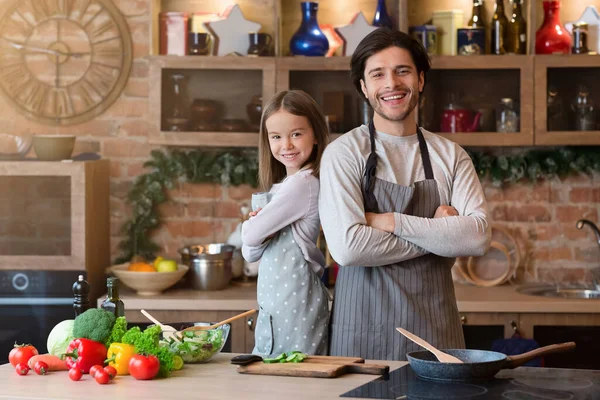 Baba ve kızı önlüklerinde poz veriyor, mutfakta birlikte yemek pişiriyorlar. — Stok fotoğraf
