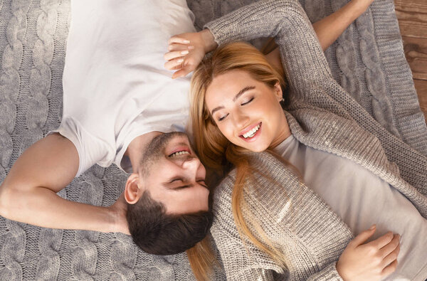 Young husband and wife lying together on knitted plaid, overhead view