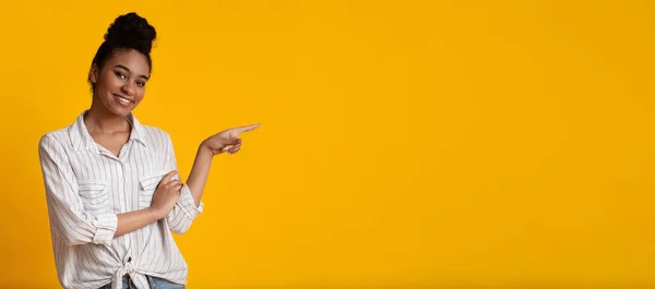 Millennial afro meisje wijzen opzij op kopieerruimte op gele achtergrond — Stockfoto