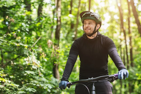 Ciclista sorridente olhando ao redor enquanto pedalava na floresta — Fotografia de Stock